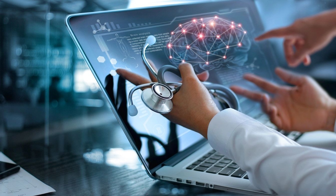 A doctor holding a stethoscope looking at an image of a brain scan on a laptop screen